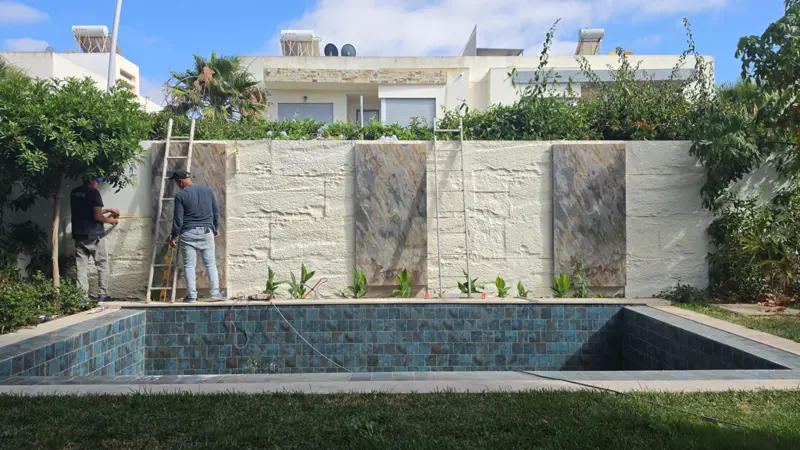 Mur d'une piscine habillé en Big Rock pendant la pose, bassin en mosaïque bleue