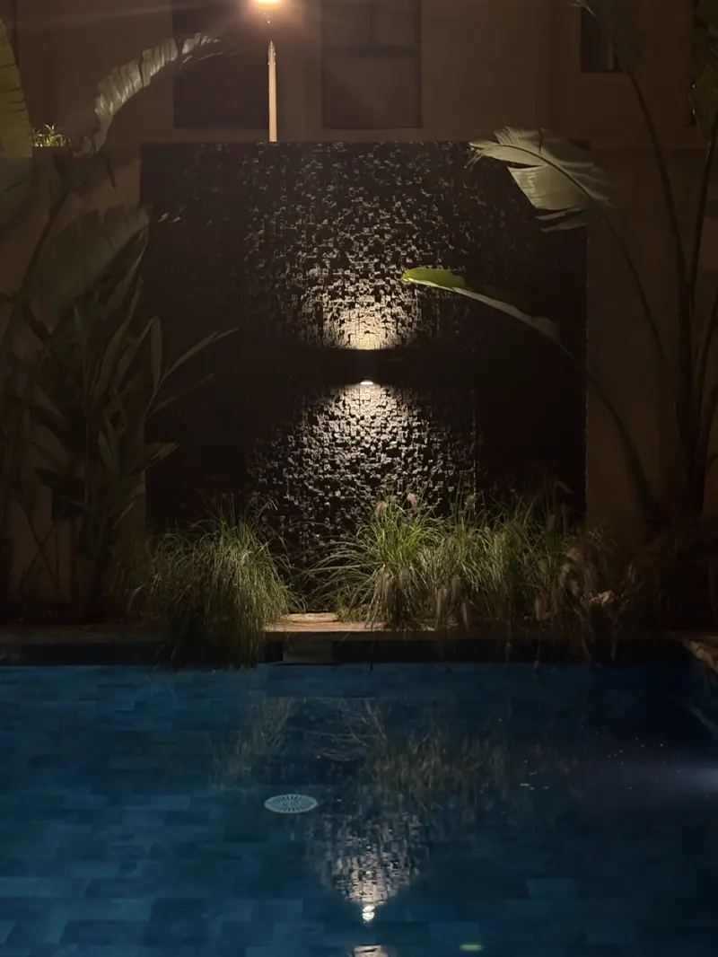 Mur d'eau de piscine habillé en Cubo, éclairé la nuit au-dessus du bassin